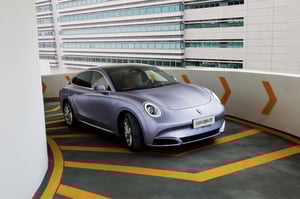 Der GWM ORA 07 GT in DreamScape Purple fährt elegant-sportlich eine enge Zufahrt zu einem Parkhaus hoch