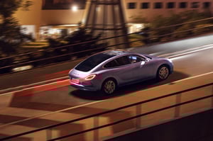 Der GWM ORA 07 GT in Dreamscape Purple braust durch eine Stadt bei Nacht. Die optischen Highlights: die Felgen, das Design der ORA typischen LED-Scheinwerfer sowie das riesige Panoramaglasdach, das sich komplett über die vorderen und hinteren Sitze hinweg bis zum Heck erstreckt
