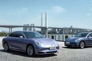 Zwei GWM ORA 07 GT in Dreamscape Purple geparkt am Ufer eines Flusses vor der beeindruckenden Kulisse einer Großstadt